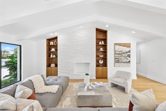 living room featuring a stone fireplace, vaulted ceiling with beams, light wood-type flooring, and built in shelves