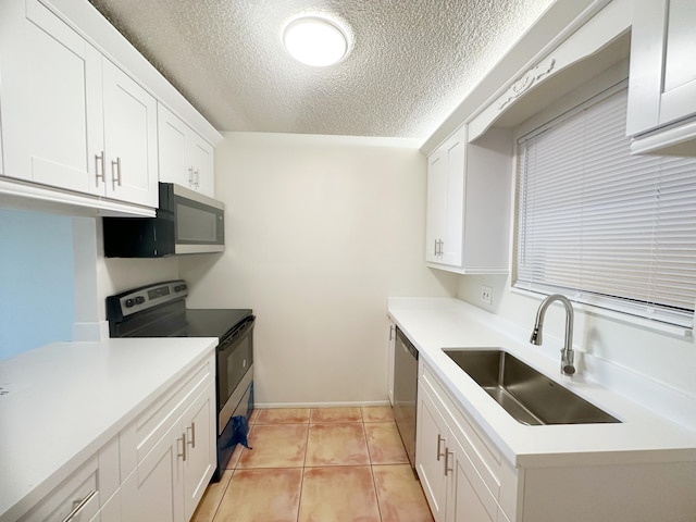 kitchen with sink, light tile patterned floors, appliances with stainless steel finishes, white cabinetry, and a textured ceiling