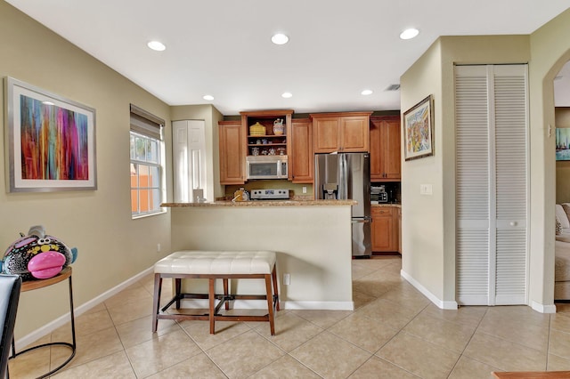 kitchen featuring appliances with stainless steel finishes, a kitchen breakfast bar, light tile patterned floors, kitchen peninsula, and light stone countertops