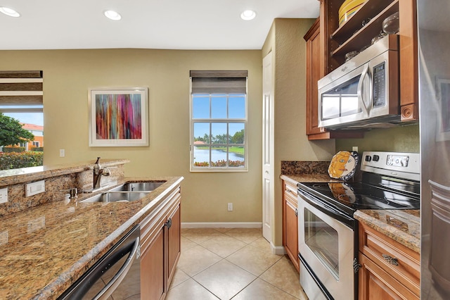 kitchen with appliances with stainless steel finishes, sink, light tile patterned floors, light stone counters, and a water view