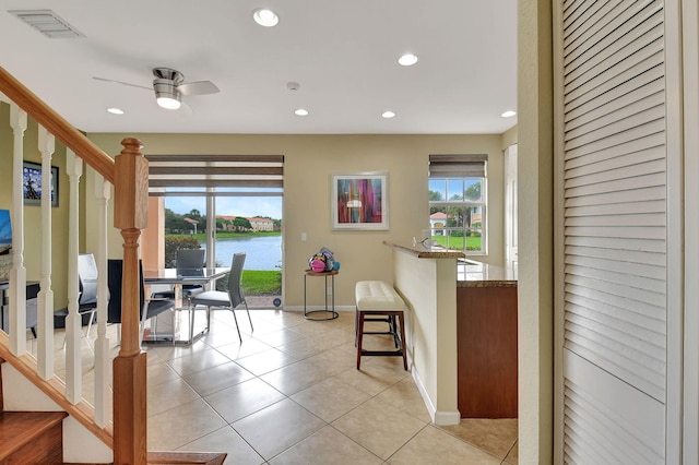 interior space with a water view, a healthy amount of sunlight, light tile patterned floors, and a breakfast bar