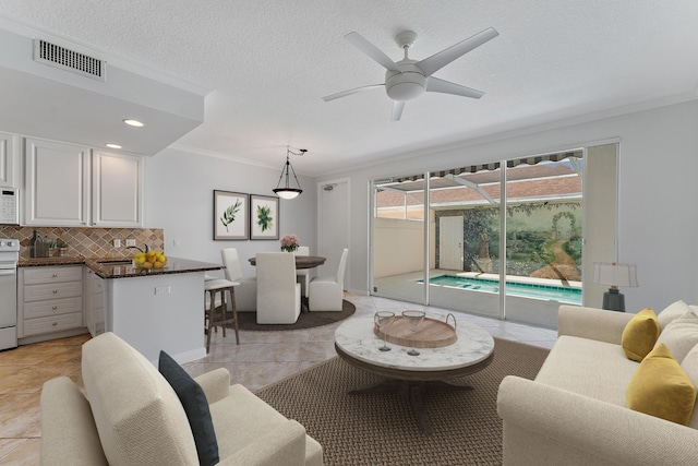 living room with light tile patterned floors, sink, ceiling fan, ornamental molding, and a textured ceiling