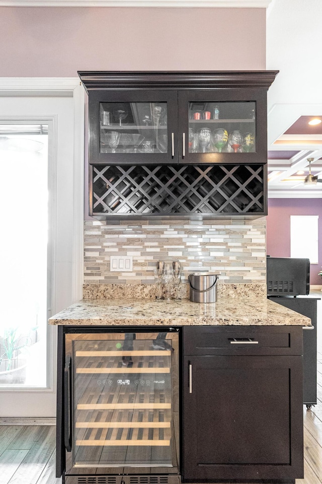 bar featuring wine cooler, light stone countertops, tasteful backsplash, and light wood-type flooring