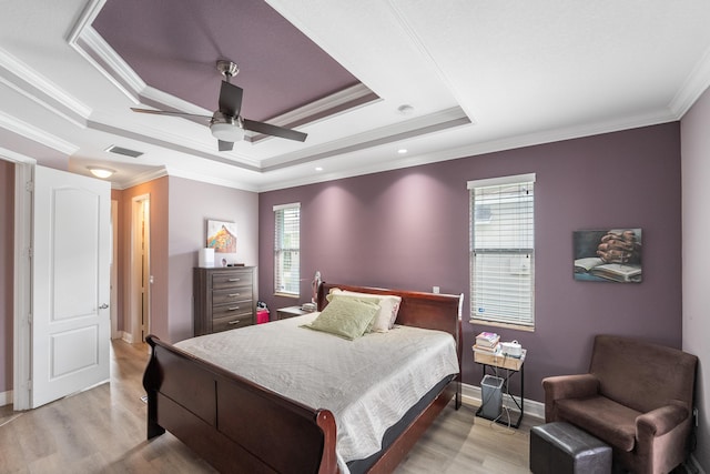 bedroom featuring multiple windows, ornamental molding, a raised ceiling, and light wood-type flooring