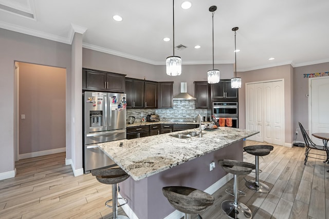 kitchen featuring appliances with stainless steel finishes, a kitchen breakfast bar, an island with sink, and wall chimney range hood