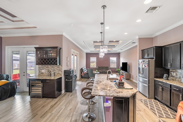 kitchen with a kitchen island with sink, hanging light fixtures, stainless steel refrigerator with ice dispenser, wine cooler, and a tray ceiling