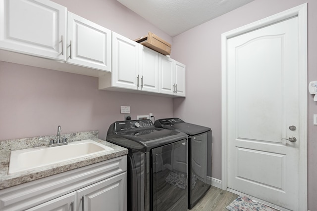 laundry area featuring sink, cabinets, washing machine and clothes dryer, a textured ceiling, and light hardwood / wood-style flooring