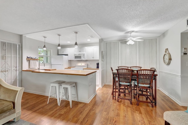 kitchen with a breakfast bar, white cabinetry, light wood-type flooring, hanging light fixtures, and white appliances