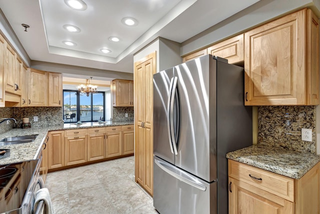 kitchen with sink, stainless steel fridge, tasteful backsplash, a tray ceiling, and light stone countertops