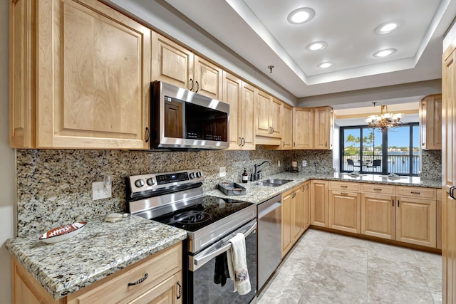 kitchen featuring sink, light stone counters, decorative light fixtures, a tray ceiling, and stainless steel appliances