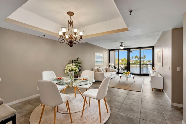 dining area featuring tile patterned flooring, a water view, expansive windows, ceiling fan with notable chandelier, and a raised ceiling