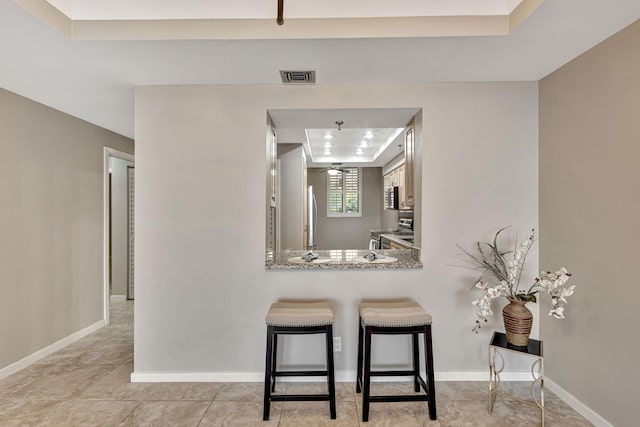 kitchen with stone counters, a breakfast bar, kitchen peninsula, stainless steel appliances, and a raised ceiling