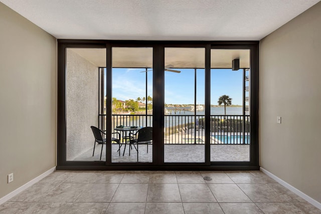 doorway with floor to ceiling windows, a water view, light tile patterned floors, and a textured ceiling