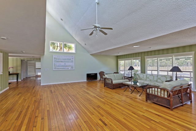 living room with ceiling fan, high vaulted ceiling, a textured ceiling, and light wood-type flooring