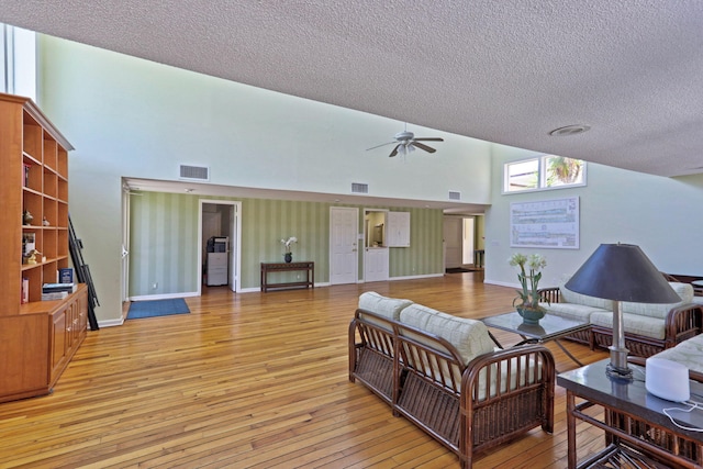 living room with ceiling fan, high vaulted ceiling, light hardwood / wood-style floors, and a textured ceiling