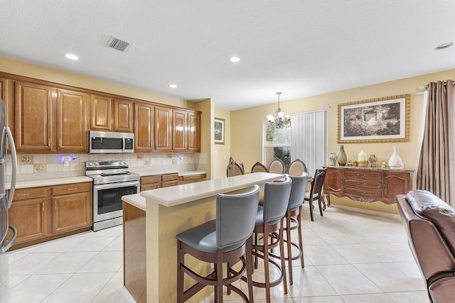 kitchen with hanging light fixtures, stainless steel appliances, a kitchen breakfast bar, and light tile patterned flooring