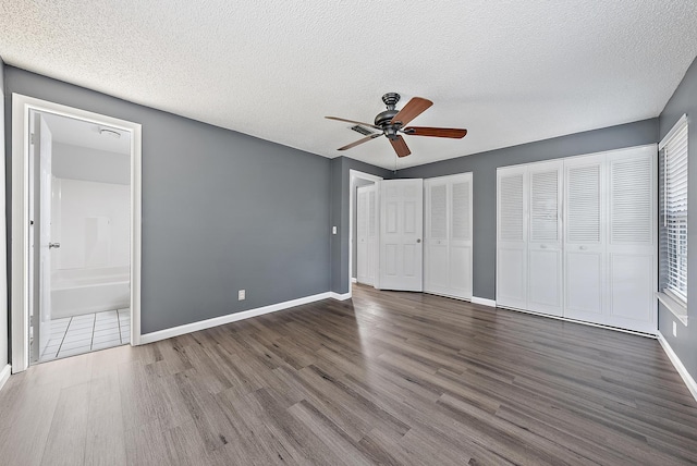 unfurnished bedroom featuring connected bathroom, a textured ceiling, dark hardwood / wood-style flooring, two closets, and ceiling fan