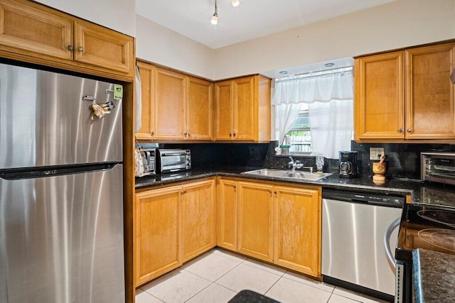 kitchen with sink, tasteful backsplash, light tile patterned floors, dark stone countertops, and appliances with stainless steel finishes