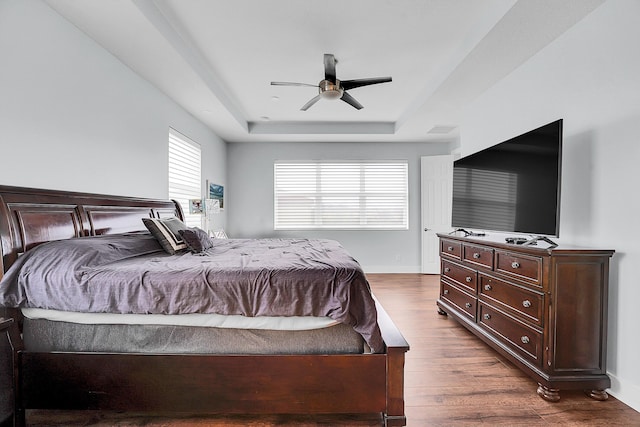 bedroom with ceiling fan, dark hardwood / wood-style floors, and a raised ceiling