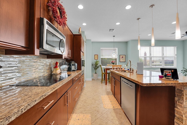 kitchen with sink, appliances with stainless steel finishes, hanging light fixtures, an island with sink, and decorative backsplash