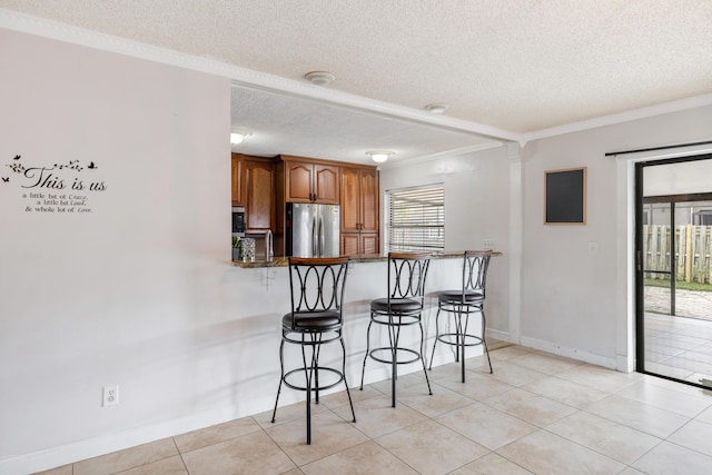 kitchen featuring stainless steel appliances, ornamental molding, a textured ceiling, a kitchen bar, and kitchen peninsula