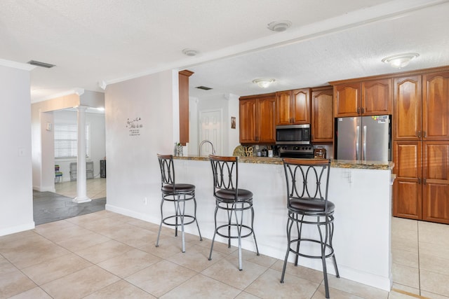 kitchen with a kitchen breakfast bar, kitchen peninsula, stone counters, stainless steel appliances, and decorative columns