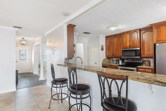 kitchen featuring light stone countertops, stainless steel appliances, kitchen peninsula, and ornate columns