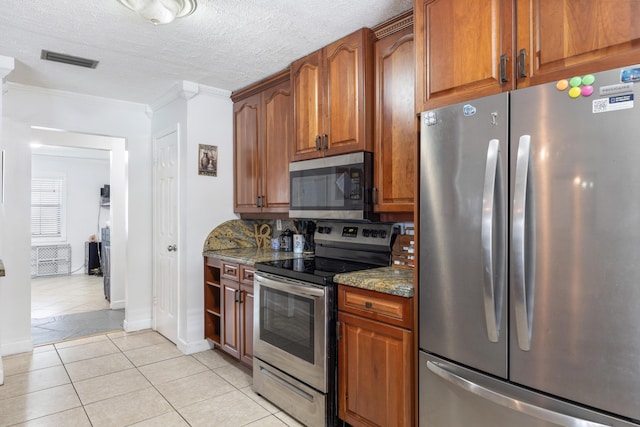 kitchen with a textured ceiling, light tile patterned floors, ornamental molding, appliances with stainless steel finishes, and stone counters