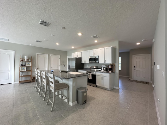 kitchen featuring a breakfast bar area, dark stone countertops, stainless steel appliances, a kitchen island with sink, and white cabinets