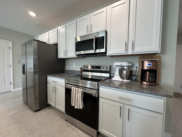 kitchen with appliances with stainless steel finishes, dark stone countertops, white cabinets, light tile patterned floors, and a textured ceiling