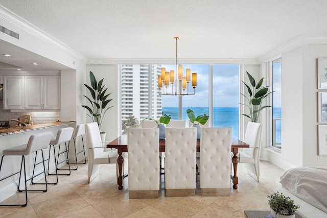 dining space featuring visible vents, ornamental molding, a water view, an inviting chandelier, and a textured ceiling