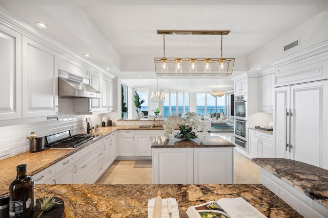 kitchen with hanging light fixtures, wall chimney range hood, white cabinetry, and stainless steel appliances