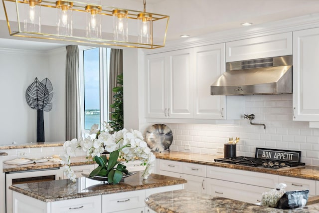 kitchen with under cabinet range hood, white cabinetry, dark stone counters, and stainless steel gas cooktop