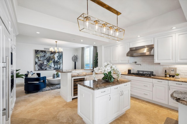 kitchen featuring stainless steel gas cooktop, a kitchen island, under cabinet range hood, white cabinetry, and pendant lighting