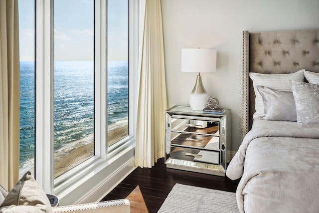 bedroom featuring dark wood-style flooring, a water view, and baseboards