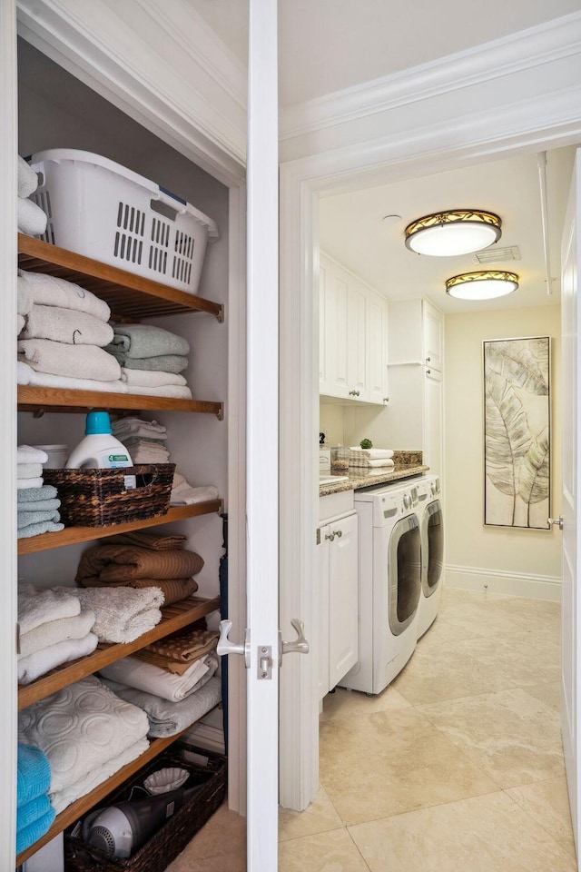 laundry area with cabinet space, light tile patterned floors, baseboards, washer and clothes dryer, and ornamental molding