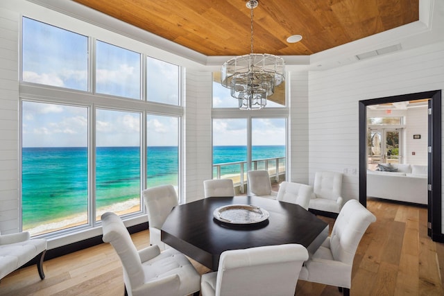 dining area with light wood-type flooring, a tray ceiling, a water view, and wood ceiling