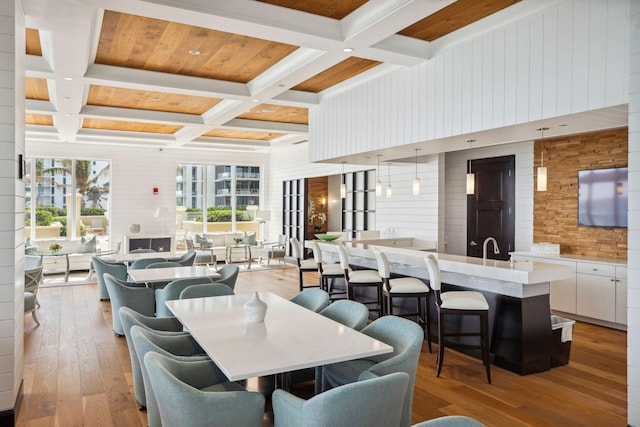 dining room featuring light wood finished floors, coffered ceiling, beam ceiling, and wood walls