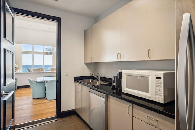 kitchen featuring stainless steel appliances, dark countertops, a water view, a sink, and dark tile patterned flooring