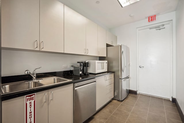 kitchen with stainless steel appliances, dark countertops, white cabinets, a sink, and tile patterned flooring