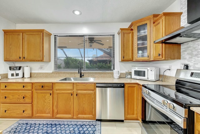 kitchen featuring sink, light tile patterned floors, ceiling fan, stainless steel appliances, and wall chimney range hood