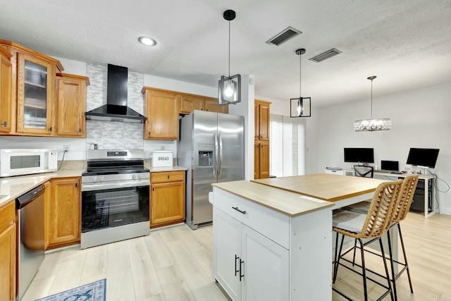 kitchen with appliances with stainless steel finishes, decorative light fixtures, decorative backsplash, and wall chimney range hood