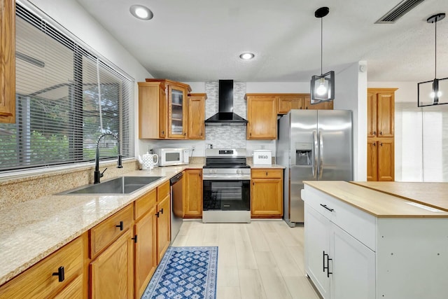 kitchen featuring pendant lighting, sink, light stone counters, stainless steel appliances, and wall chimney range hood