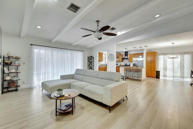 living room featuring a healthy amount of sunlight, ceiling fan with notable chandelier, light hardwood / wood-style flooring, and vaulted ceiling with beams