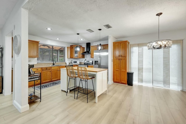 kitchen with a breakfast bar area, hanging light fixtures, stainless steel appliances, a center island, and wall chimney exhaust hood