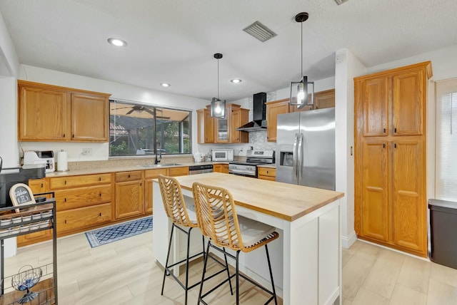 kitchen featuring sink, appliances with stainless steel finishes, a center island, decorative light fixtures, and wall chimney exhaust hood