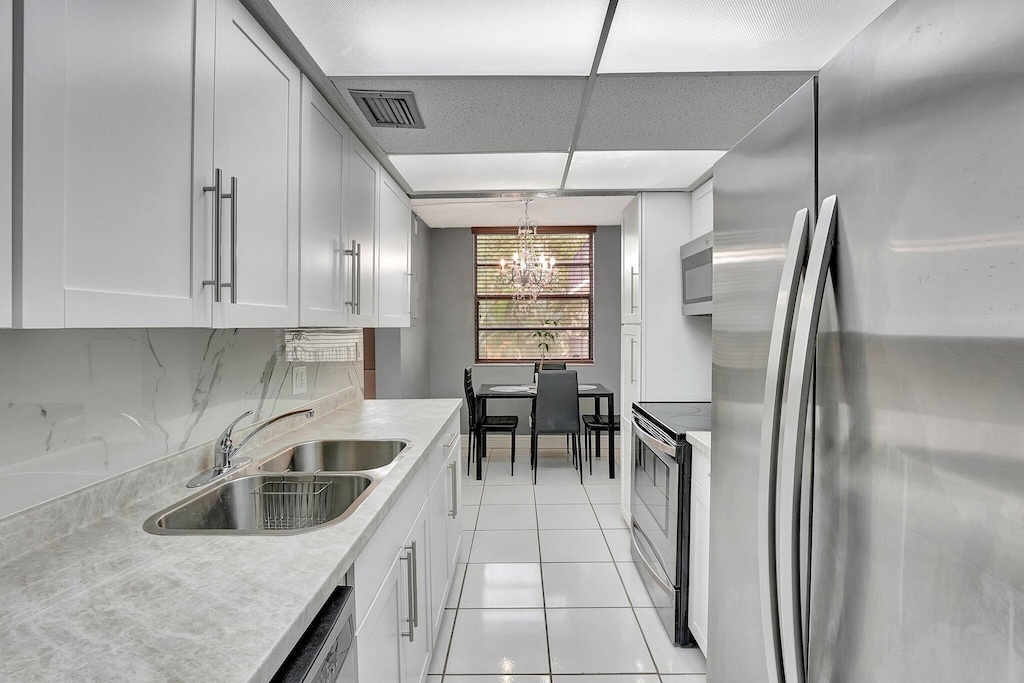 kitchen featuring light tile patterned flooring, sink, hanging light fixtures, stainless steel appliances, and light stone countertops