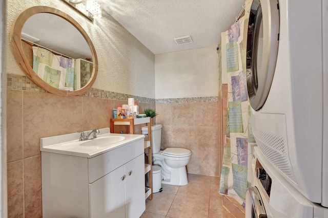 bathroom with tile patterned floors, stacked washer and clothes dryer, a textured ceiling, tile walls, and vanity