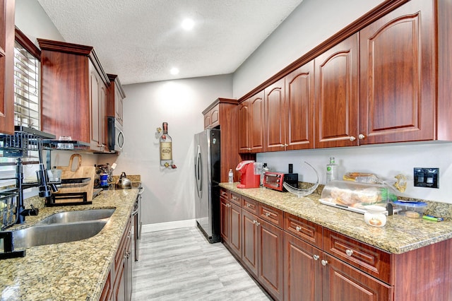 kitchen featuring appliances with stainless steel finishes, light wood-style floors, a sink, a textured ceiling, and light stone countertops