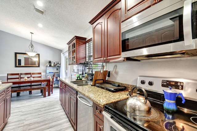 kitchen with light wood-style flooring, vaulted ceiling, appliances with stainless steel finishes, light stone countertops, and glass insert cabinets